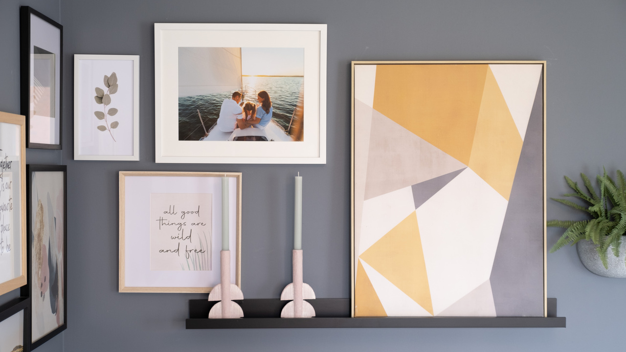 A blue wall featuring differently sized artworks and two candles on a shelf