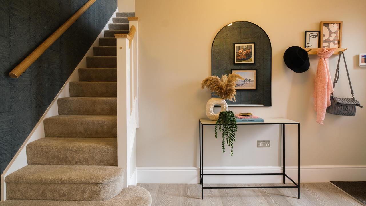 Hallway with carpeted stairs, table, arched mirror and coat hooks
