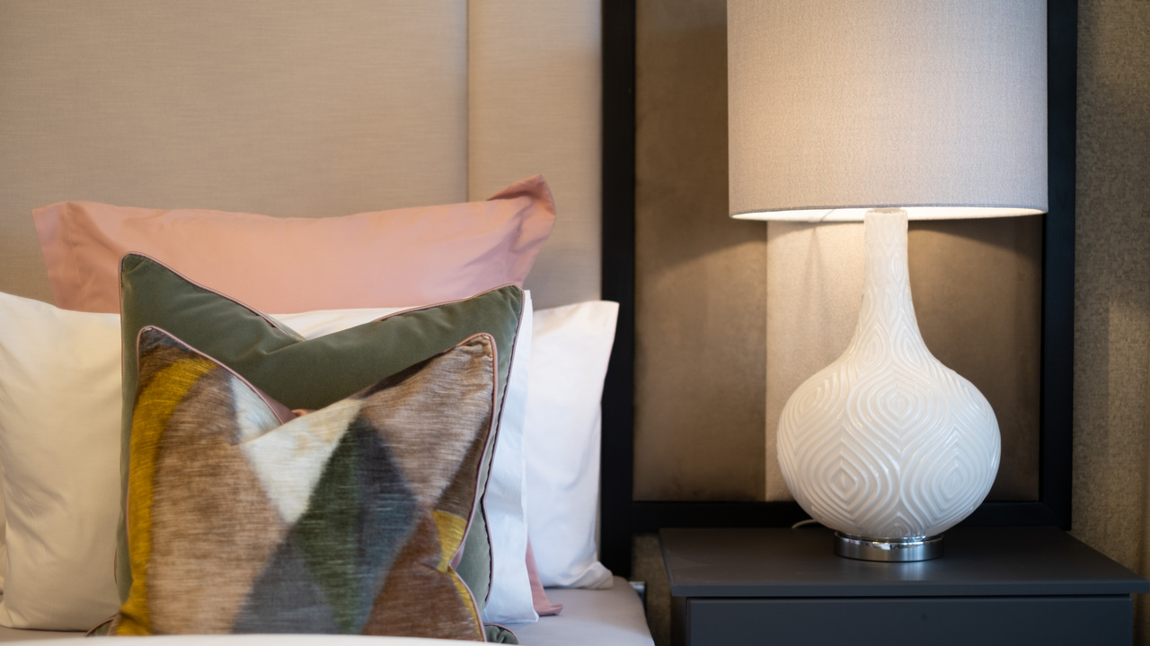 Velvet cushions on a bed, next to a bedside table with textured lamp on top