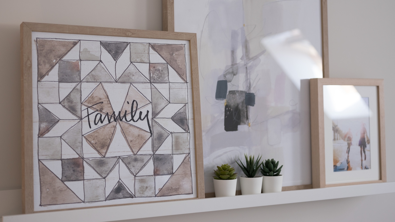 Picture rail holding three small plants and three pictures in wooden frames