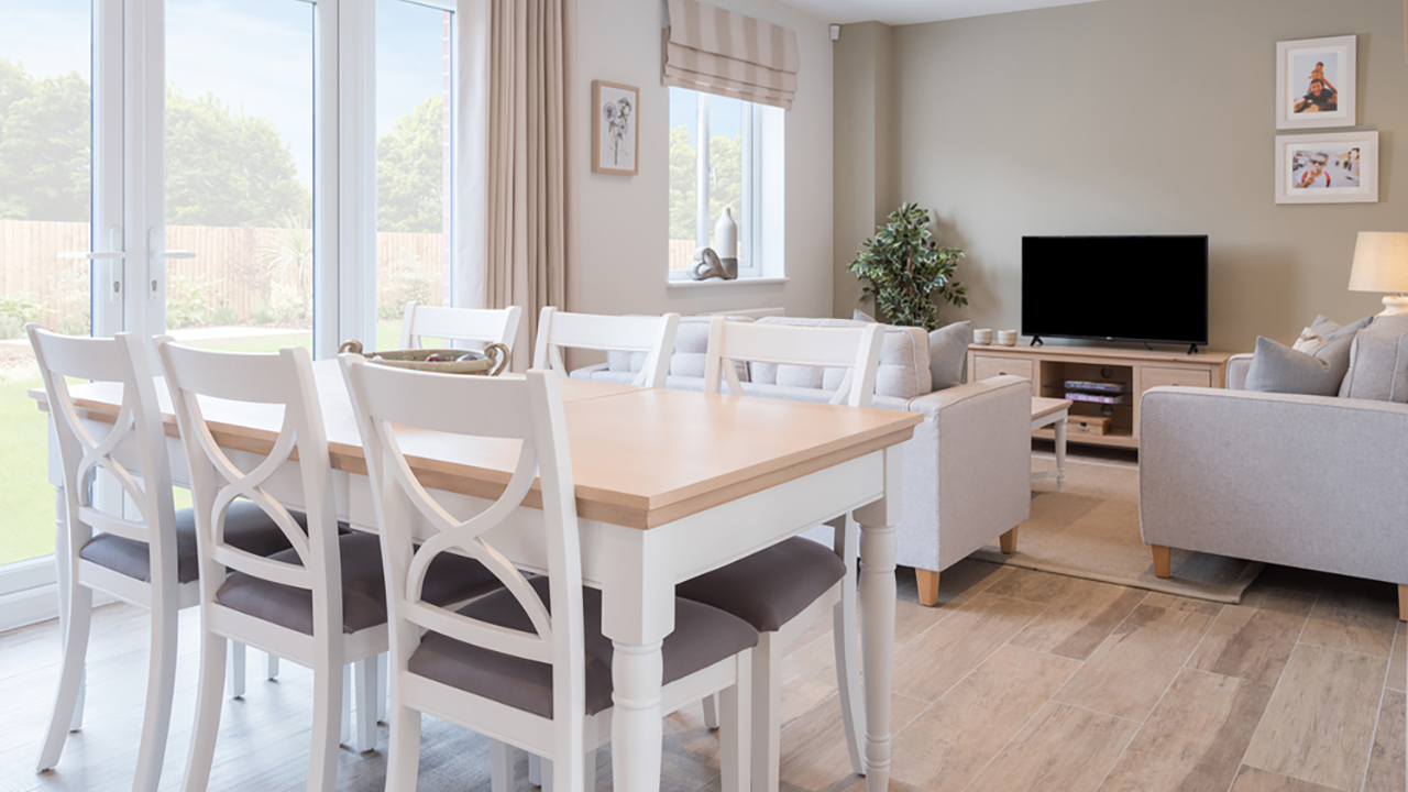 White dining table and chairs with a light wood top in front of a cosy family area