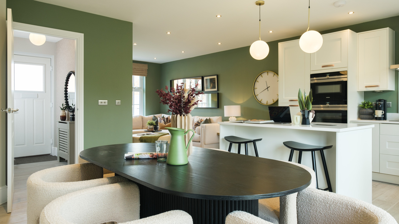 Open plan kitchen, dining and family area with sage green walls and cream tub chairs