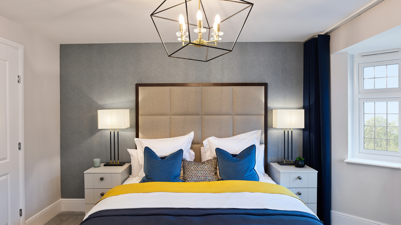 Double bed with blue and yellow accessories and a large padded headboard. A dramatic feature pendant light-fitting hangs over the bed.