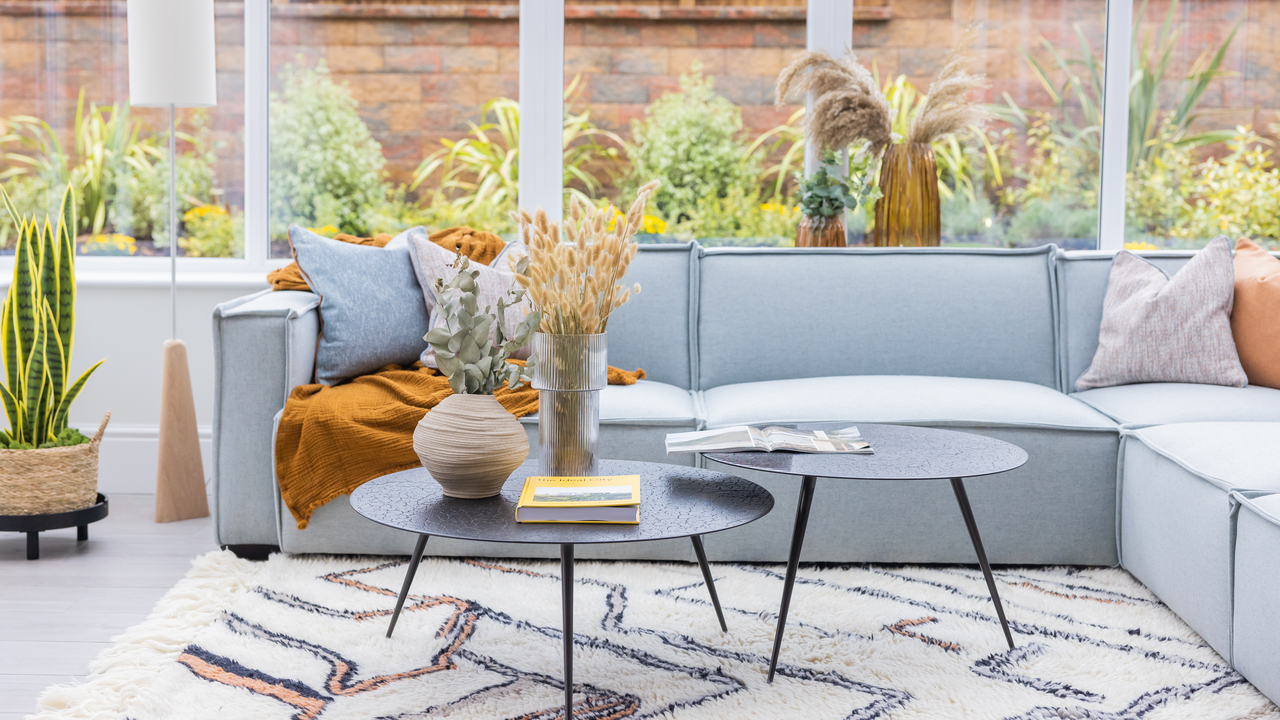 Light blue sofa and black circular nesting tables in a conservatory surrounded by plants