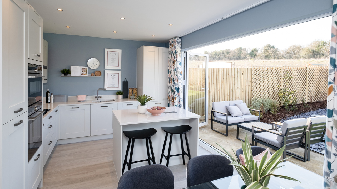 Kitchen with white units and blue walls. The bi-fold doors are open, showing the garden.