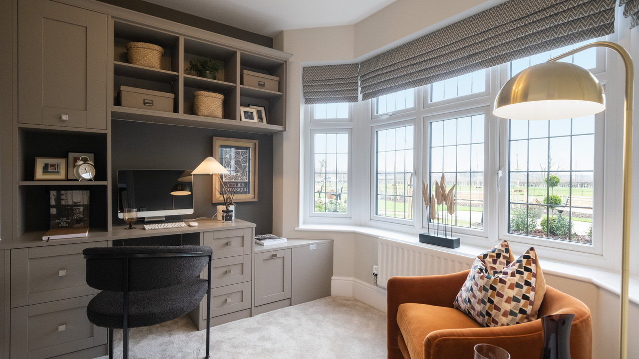 Home office with fitted desk and storage, a large bay window and an orange reading chair