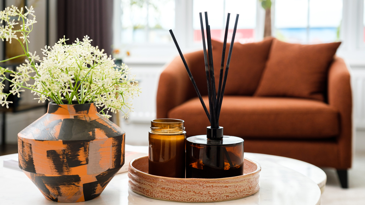 Boho vase and tray containing reed diffusers on a coffee table. An orange lounge chair sits in a bay window.