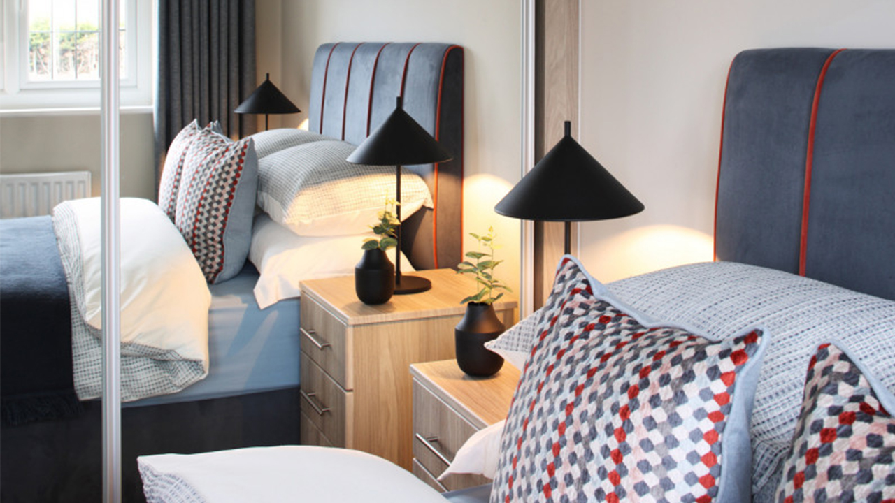 Bed with blue sheets and headboard reflecting in mirrored wardrobes