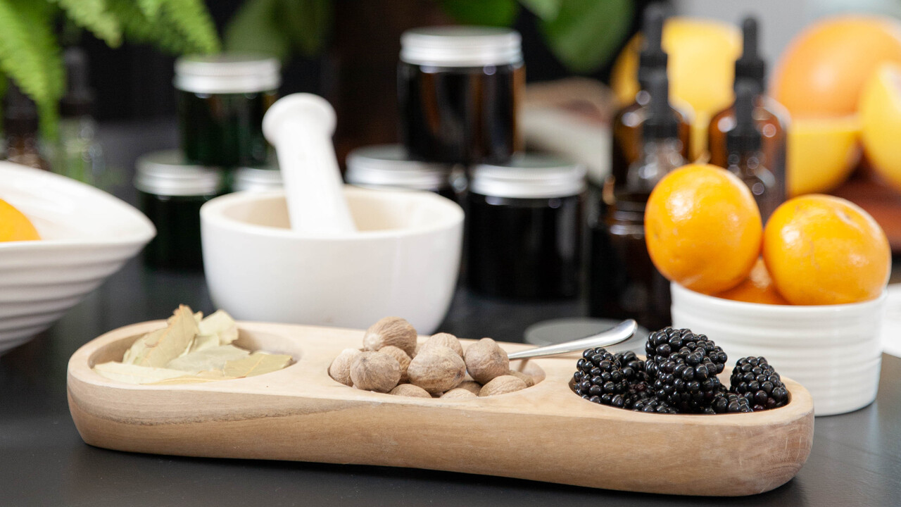Wooden tray with holes containing nuts and brambles, alongside a pestle and mortar and an orange