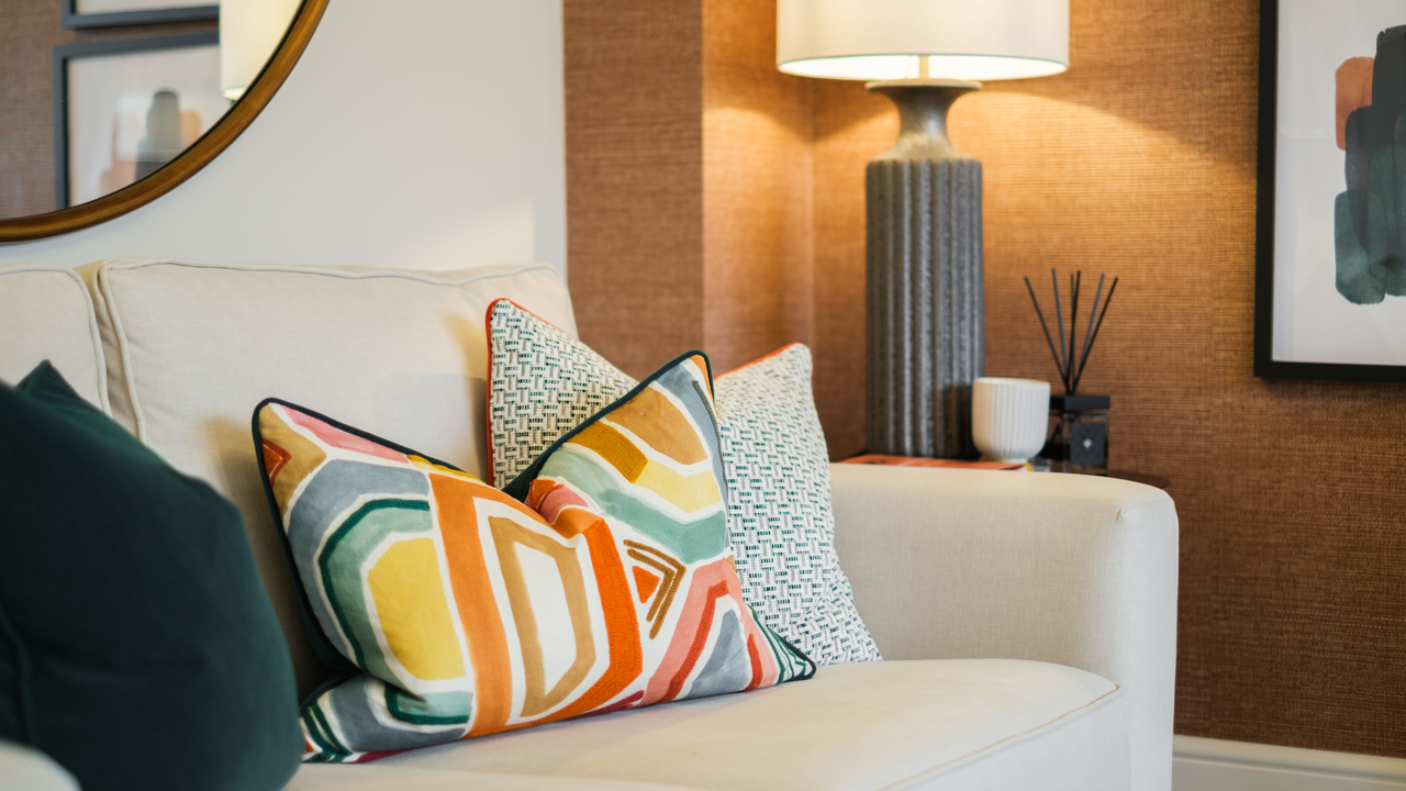 Colourful cushions on a cream sofa, next to a large lamp