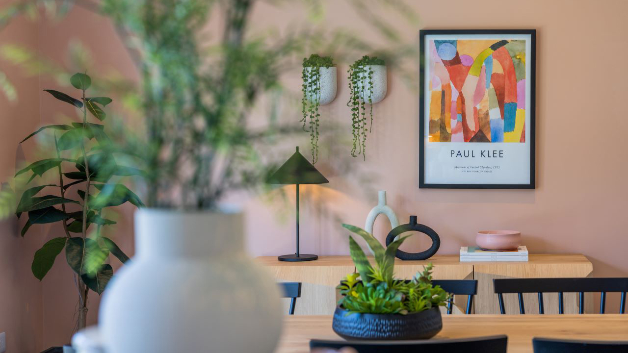 Abstract artwork on a peach-coloured wall in a dining room with lots of plants