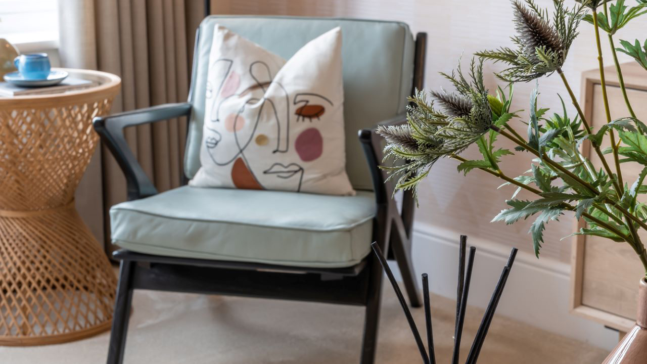 Pale blue accent chair with black wood frame and a cushion featuring an abstract face design