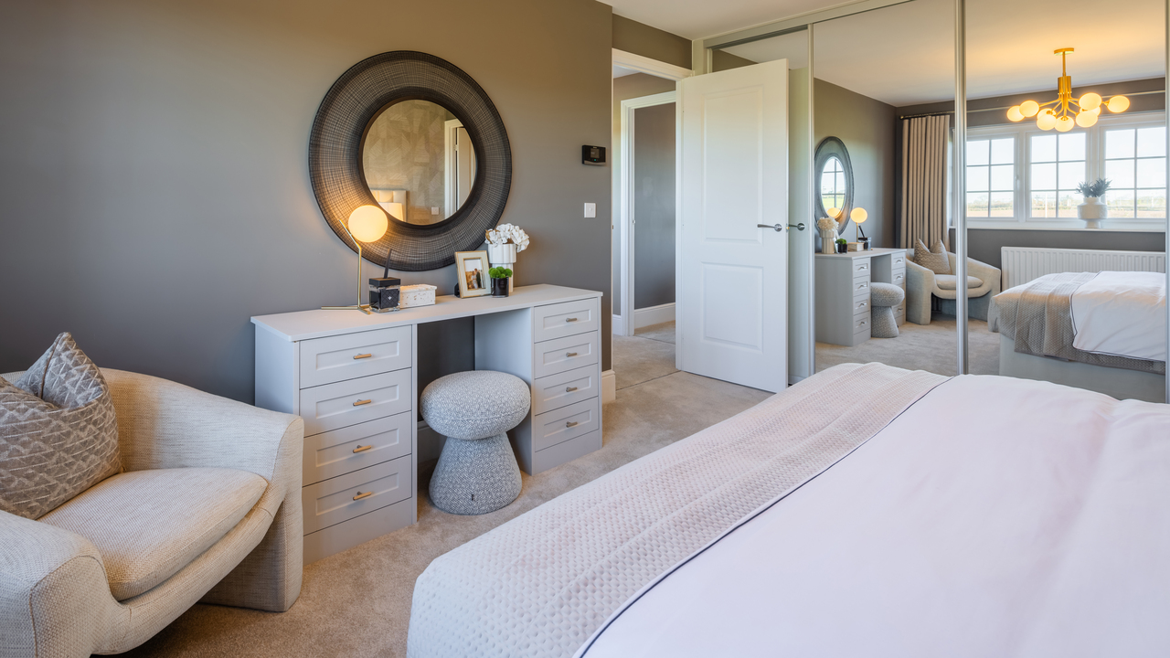 Dressing table with a round, wall-mounted mirror, next to a cream chair and mirrored wardrobes