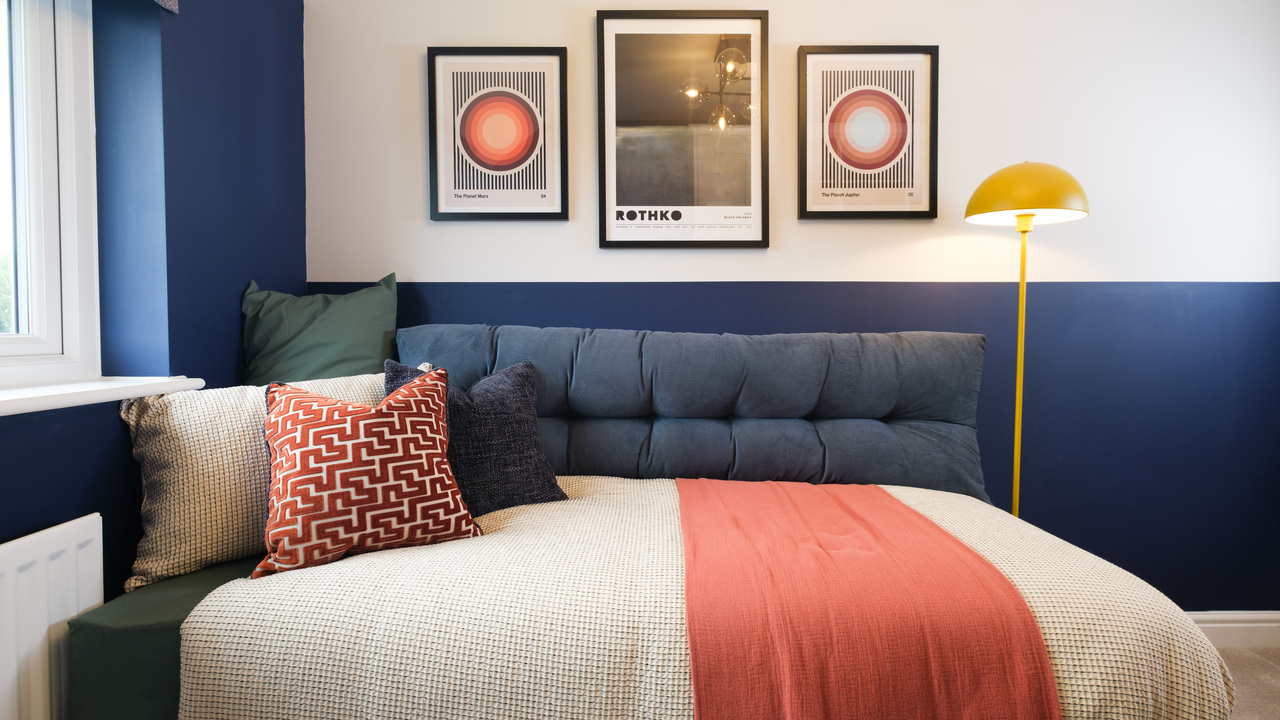 Navy sofa bed against a wall featuring three framed artworks. Next to the sofa bed is a yellow standing lamp.
