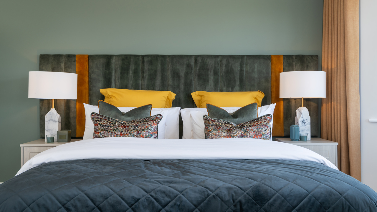 Double bed with a blue comforter and ochre accessory cushions