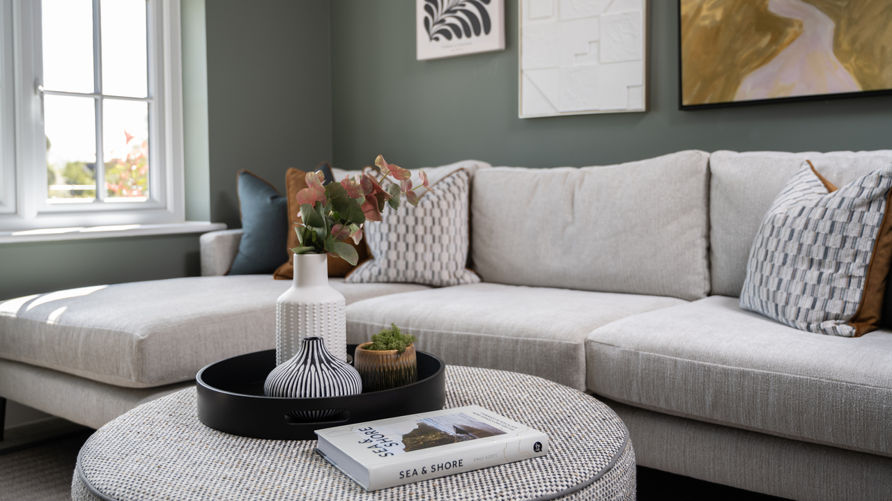Beige corner sofa with a grey tweed foot pouffe which has a tray of stylish accessories on top