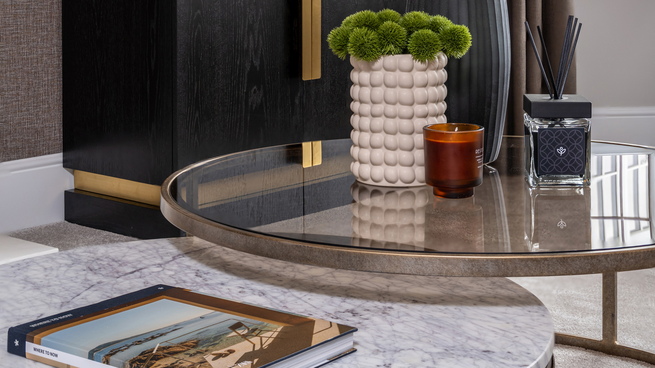 Glass and marble nesting tables with a Redrow branded scent diffuser and plant on top