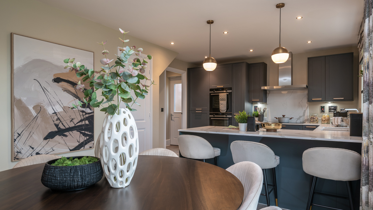 Round dining table with a large vase holding eucalyptus leaves and a navy kitchen in the background