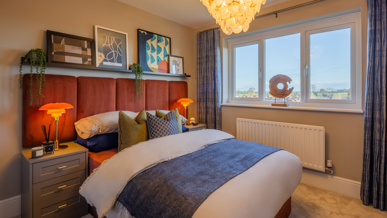 Double bedroom with padded orange headboard and a selection of framed artworks on a shelf