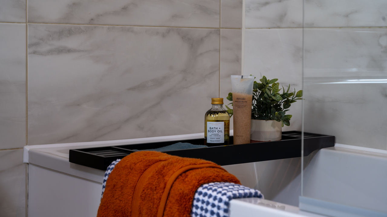 Bath with black bath tray and orange towel draped over the edge