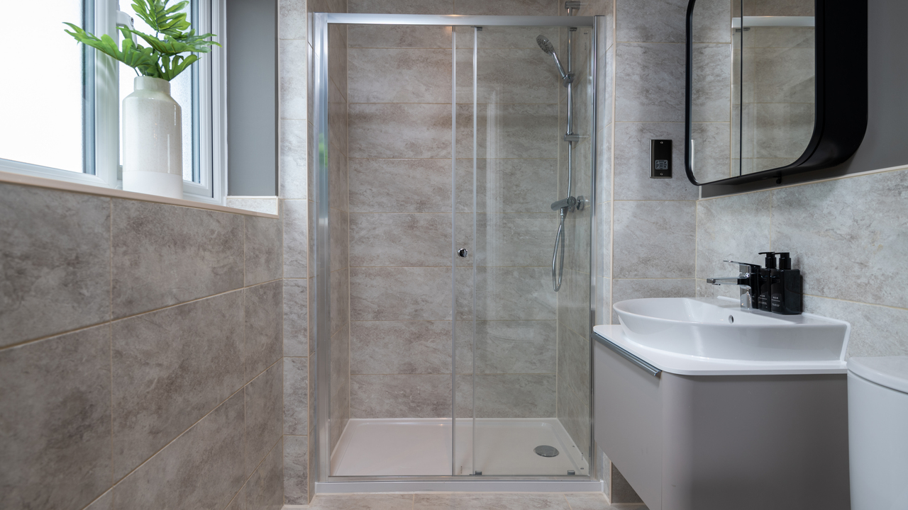 Grey tiled bathroom with shower area behind a glass screen