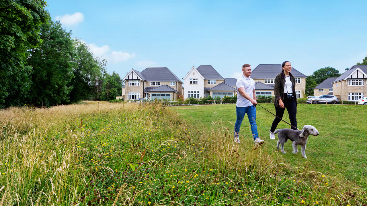 Two men walking their dog in a green area next to a Redrow development