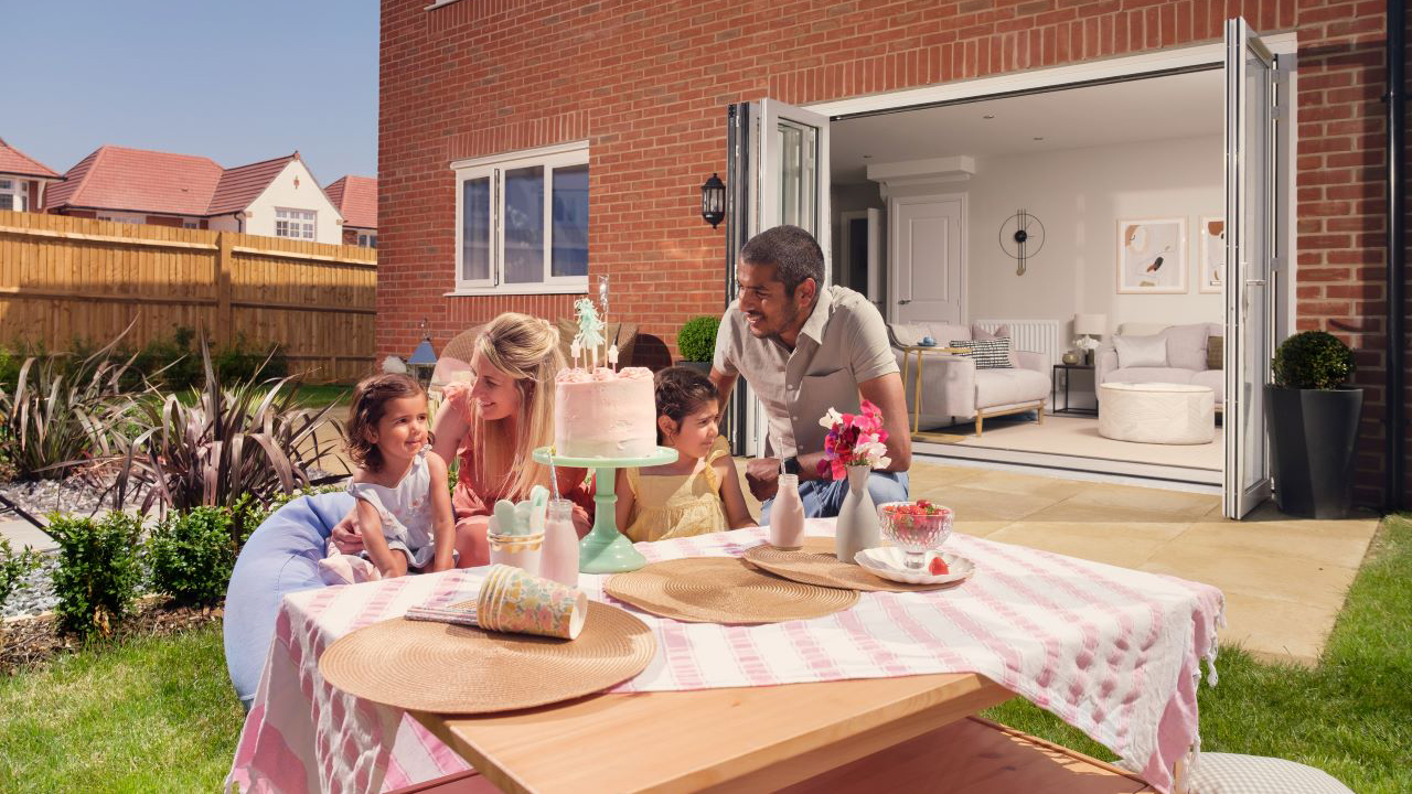 Family eating cake in the garden. Their bifold doors are open, showing the open plan living space in their home.