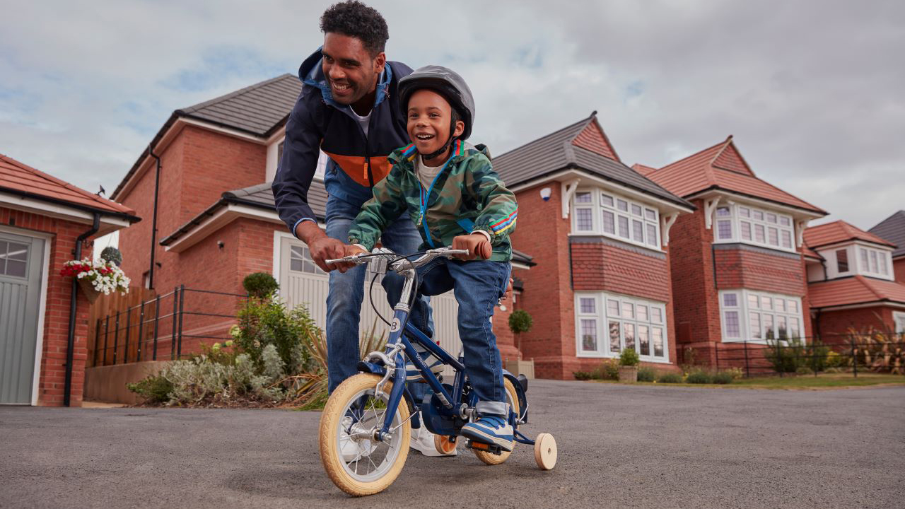 Father teaches son to ride a bike on a Redrow development