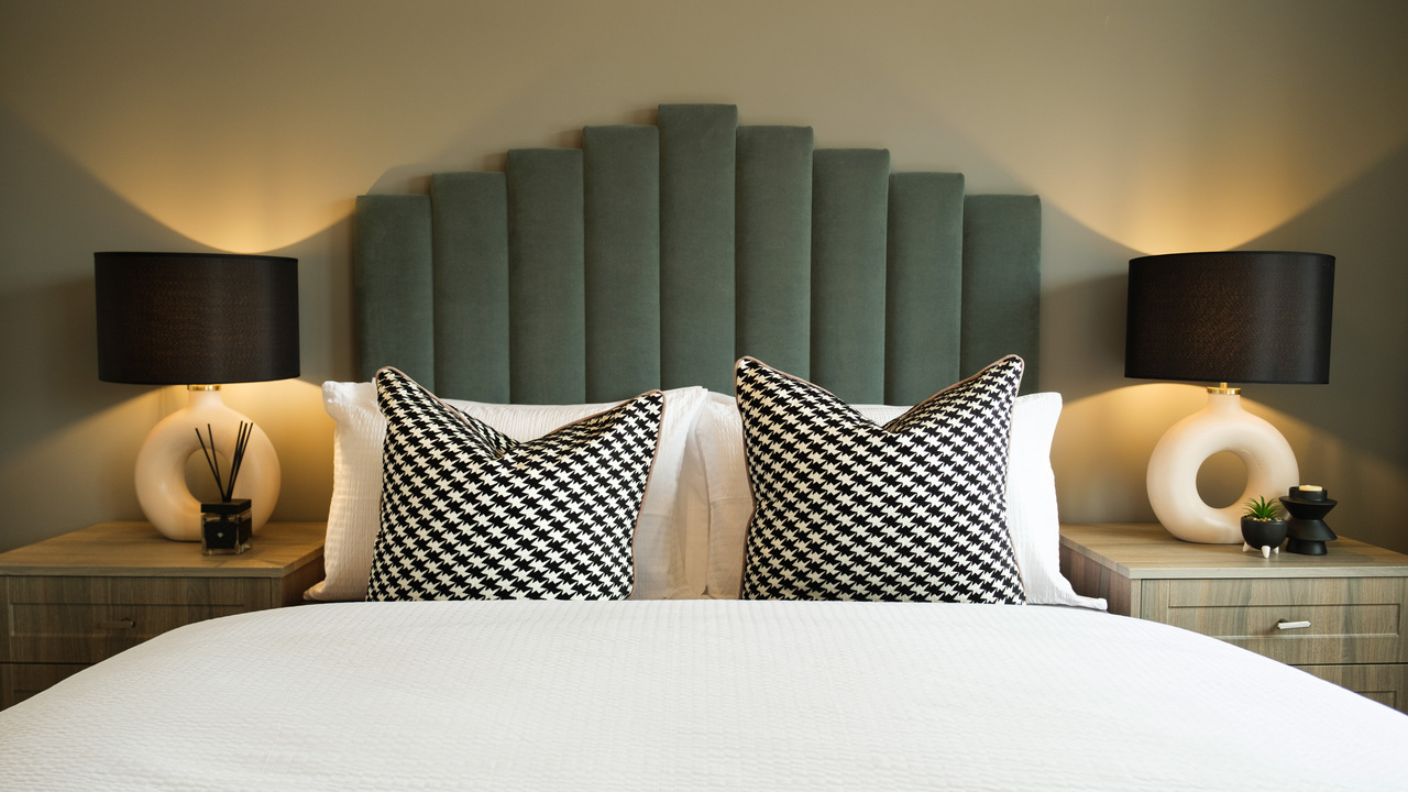 Luxurious bed with padded green headboard and matching geometric lamps