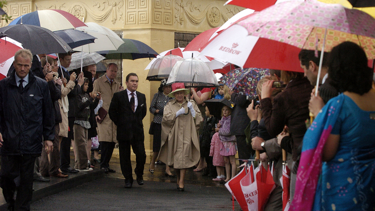 Queen Elizabeth walking through a crowd with umbrellas at Knightstone Island