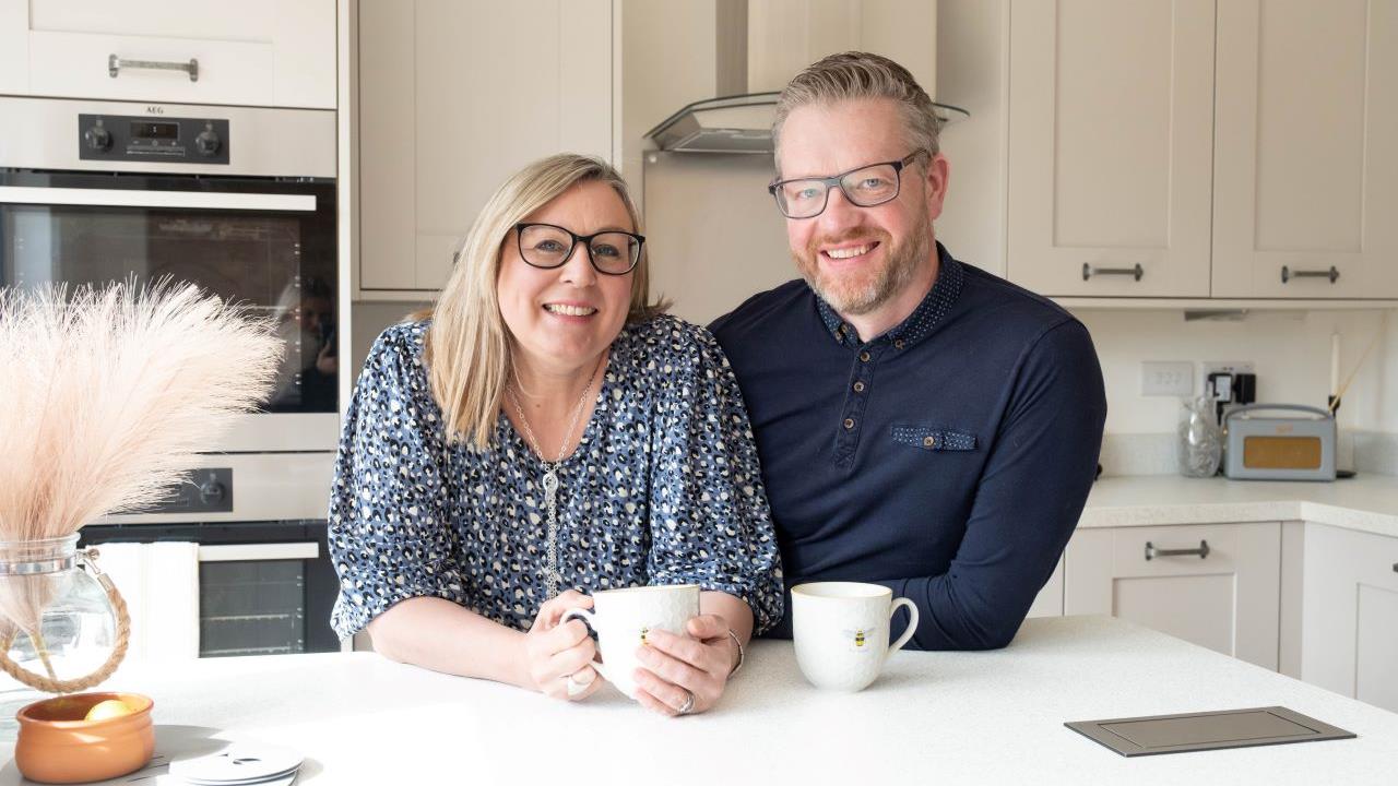 Couple holding cups of tea and smiling in their Redrow kitchen