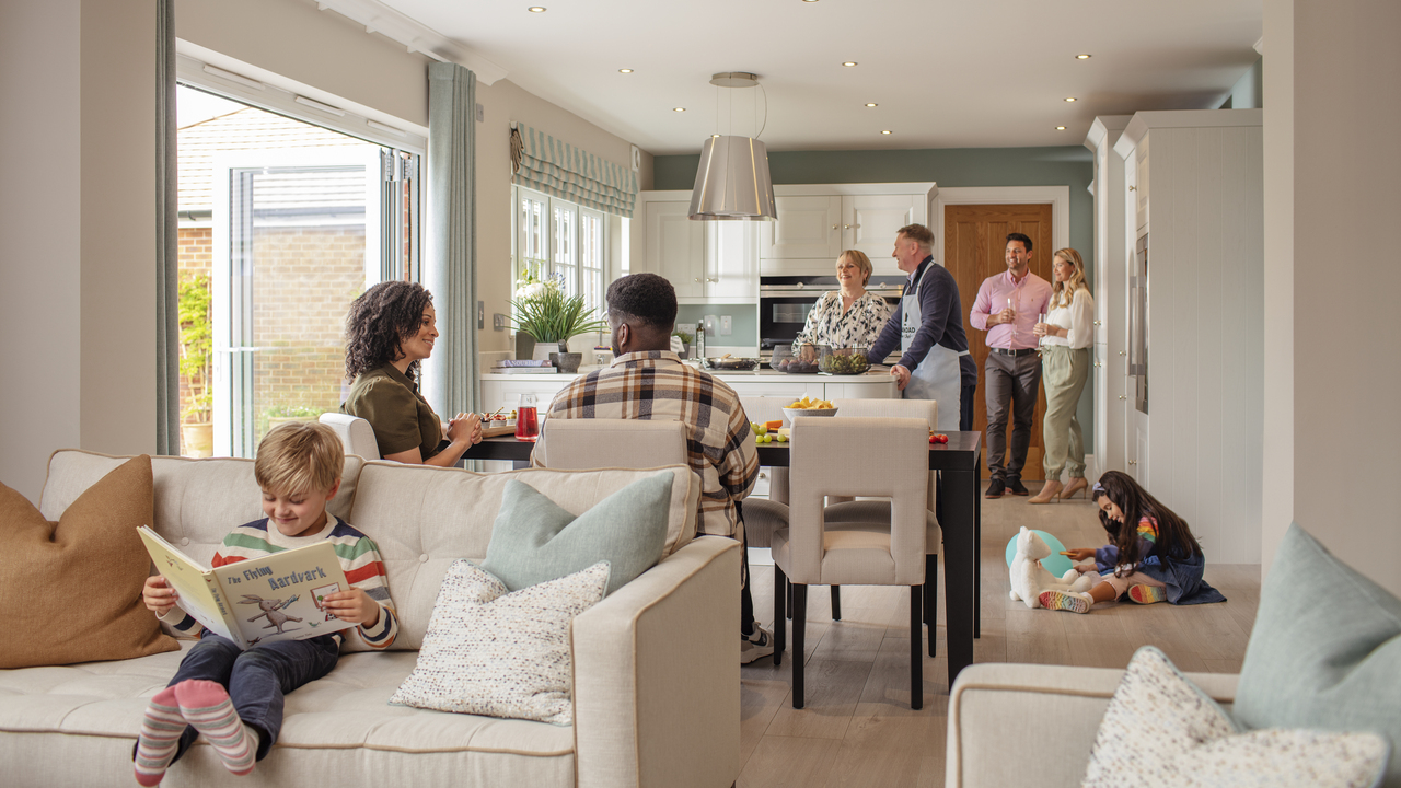 Three couples in a kitchen talking while children read books and play with toys