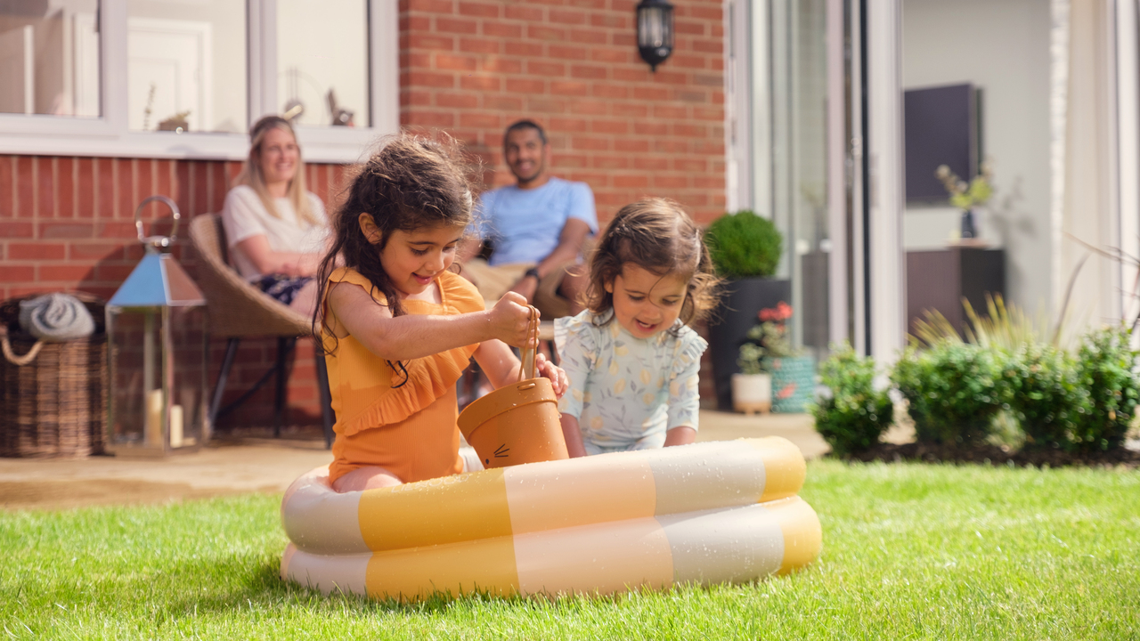 Parents relaxing while children play in a paddling pool