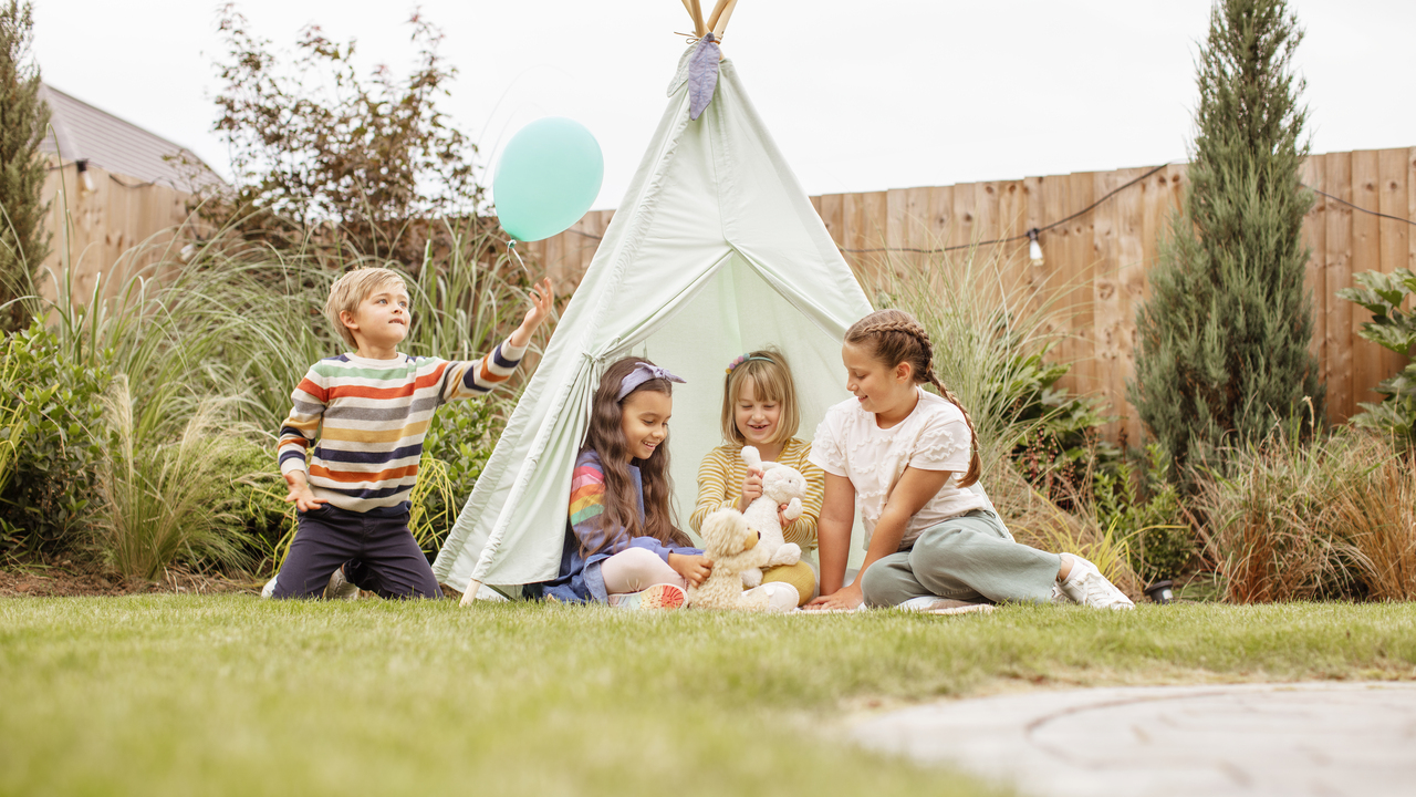 Children sat in garden with toys balloon and tent