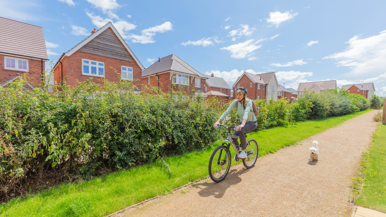 Woman cycling next to dog down a cycle path in a Redrow development
