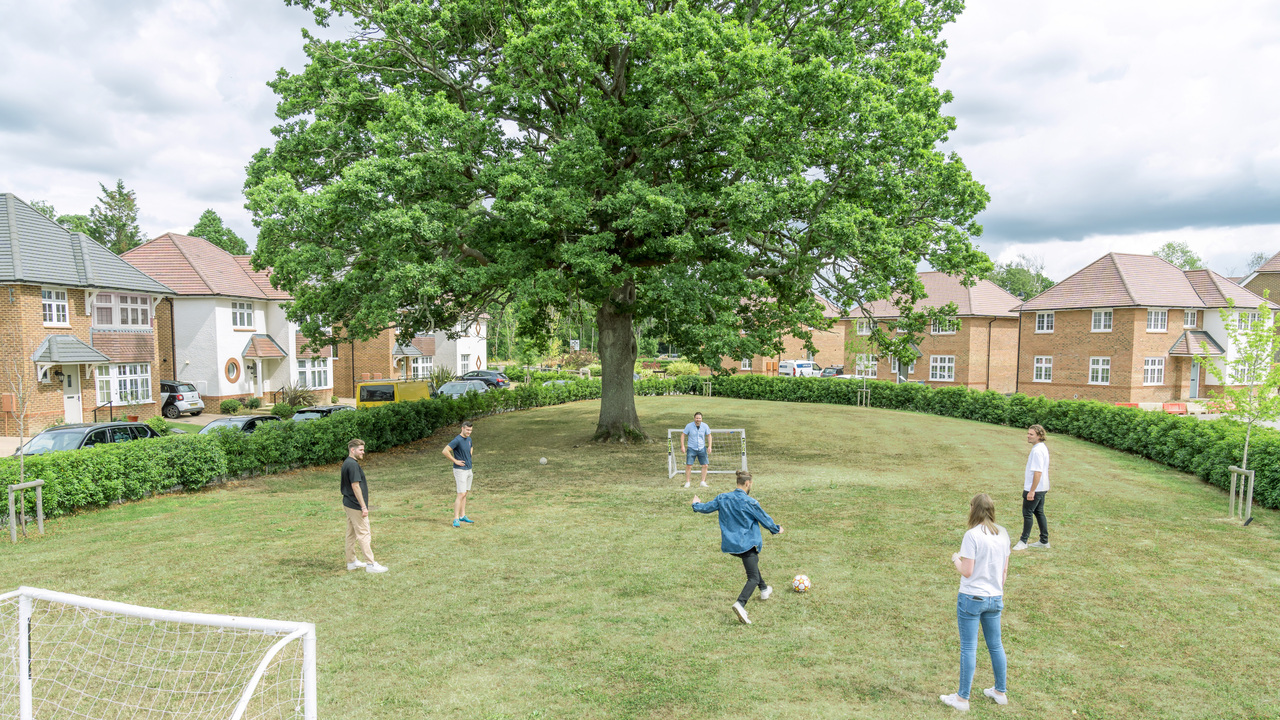 People playing football on some green space in the middle of a Redrow development.
