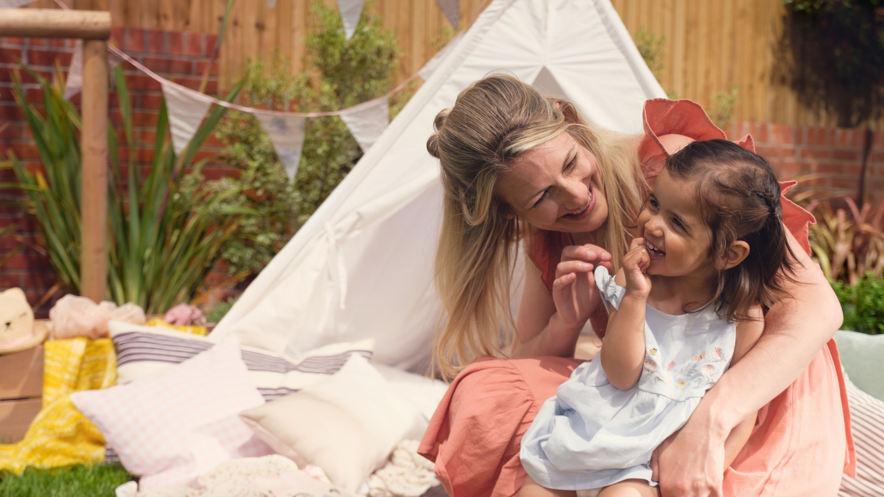 Mother and child laughing in a garden with a tipi and bunting behind them