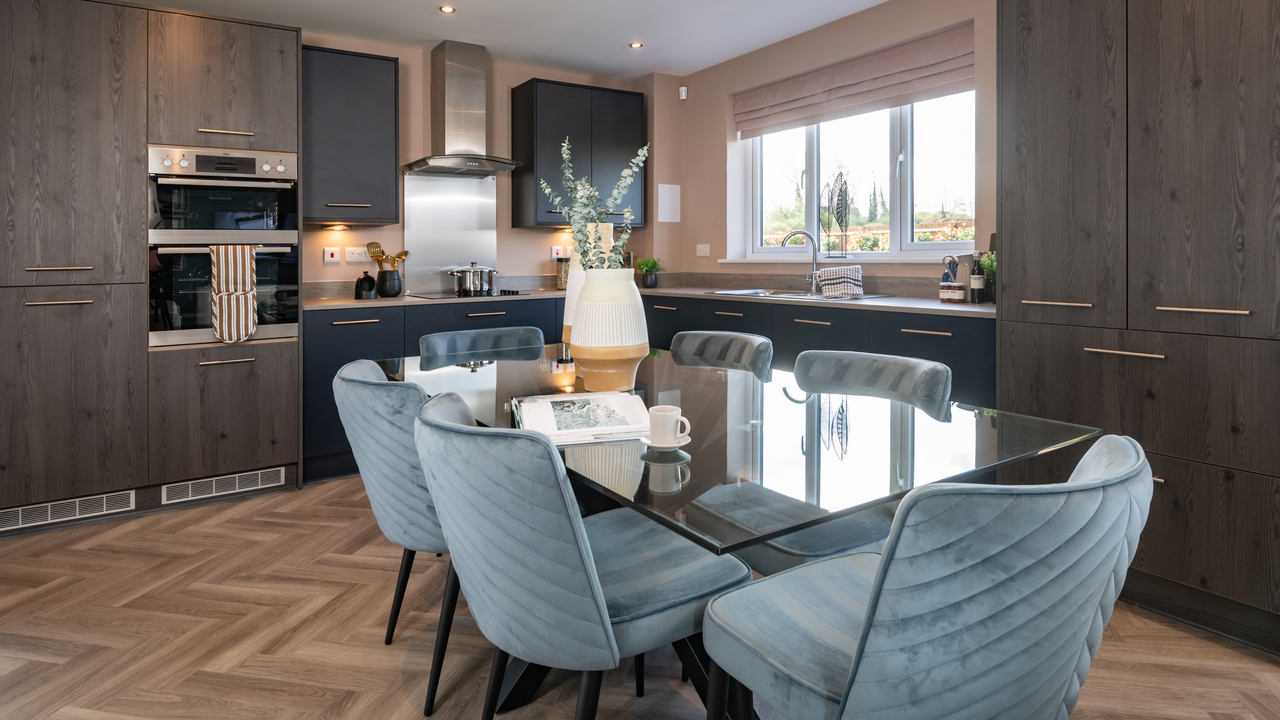 Modern dark wood kitchen with parquet flooring and a glass dining table in the middle with pale blue velvet chairs