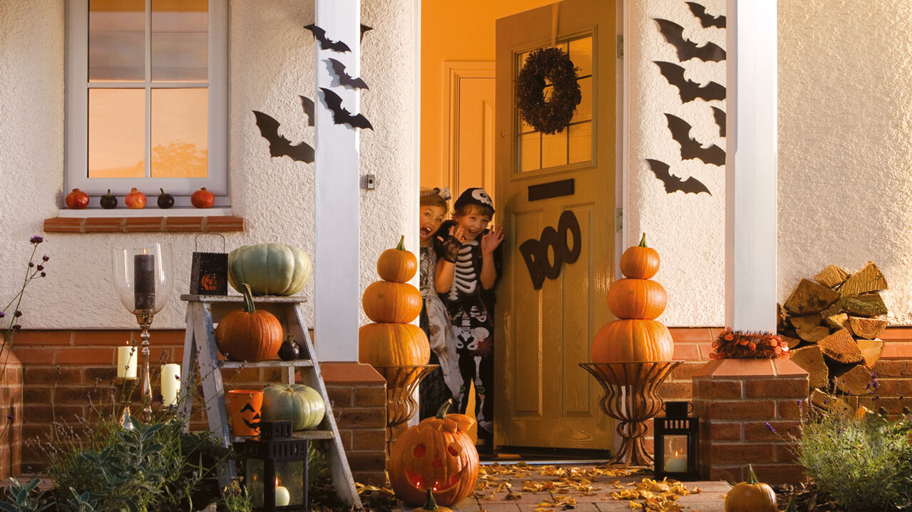 Two children in fancy dress peeking out of their door and pulling faces 