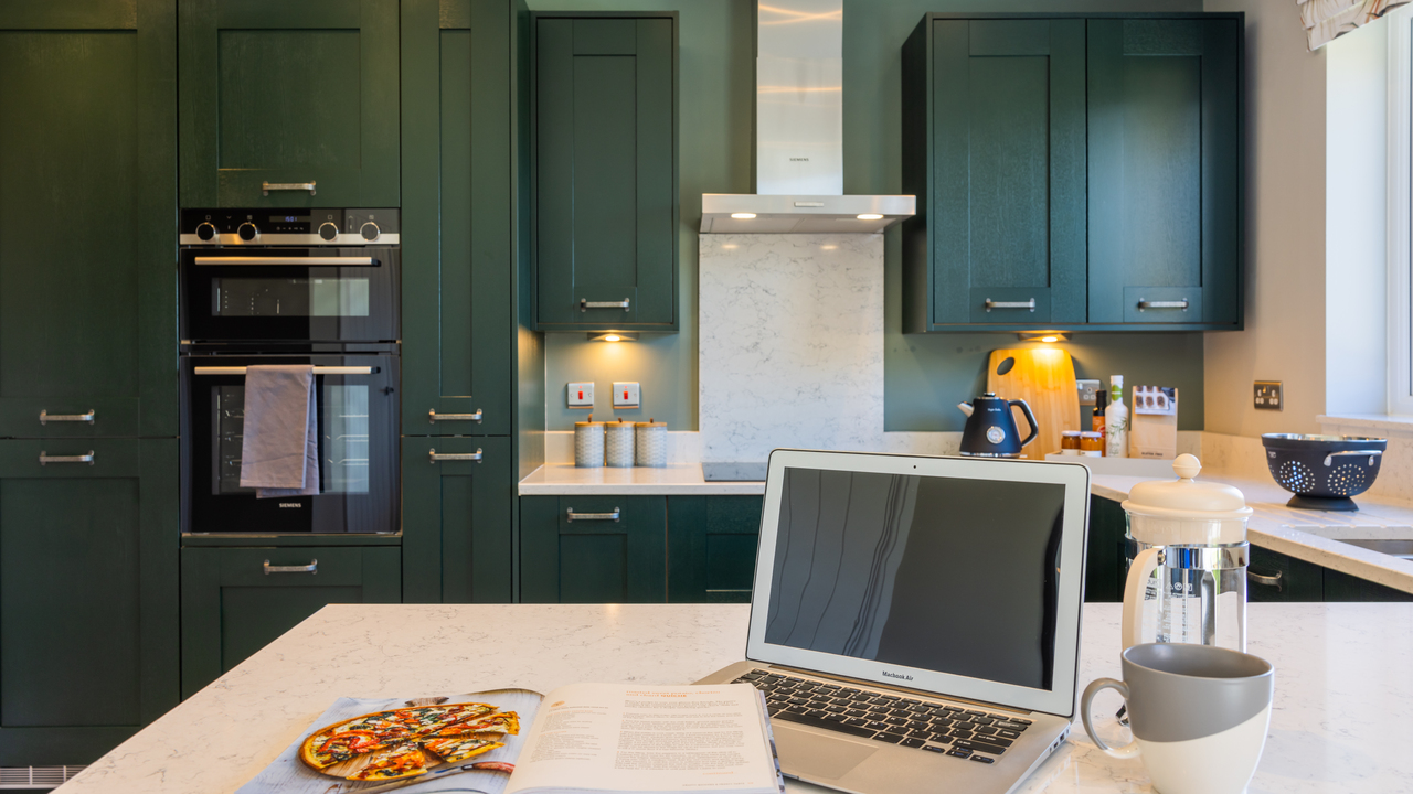 Laptop on the breakfast bar in a stylish kitchen with dark blue units