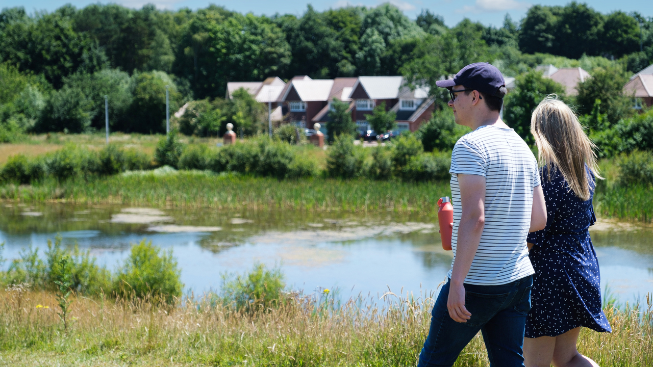 Couple walking by a pond surrounded by greenery