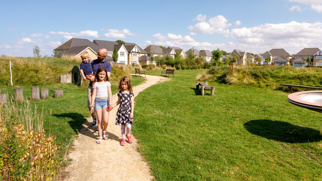 Family walking down a path surrounded by trees and grass, with a Redrow development visible in the background