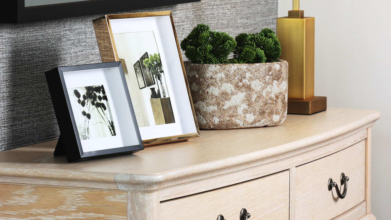 Light wood chest of drawers with framed pictures and plants on top