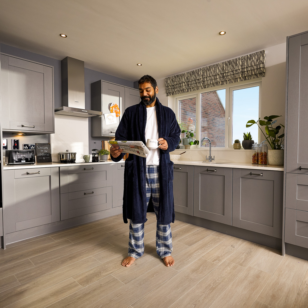 Man reading paper barefooted in kitchen